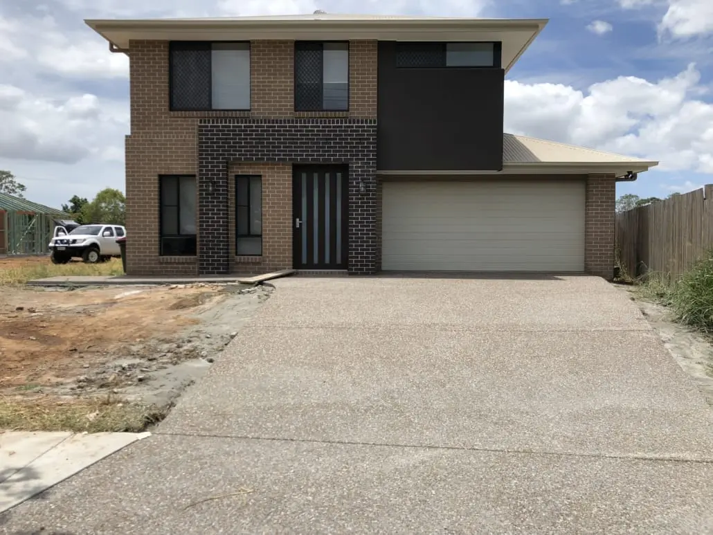 Exposed aggregate concrete driveway in front of a new two-storey brick home, honey and grey stone washed back and sealed