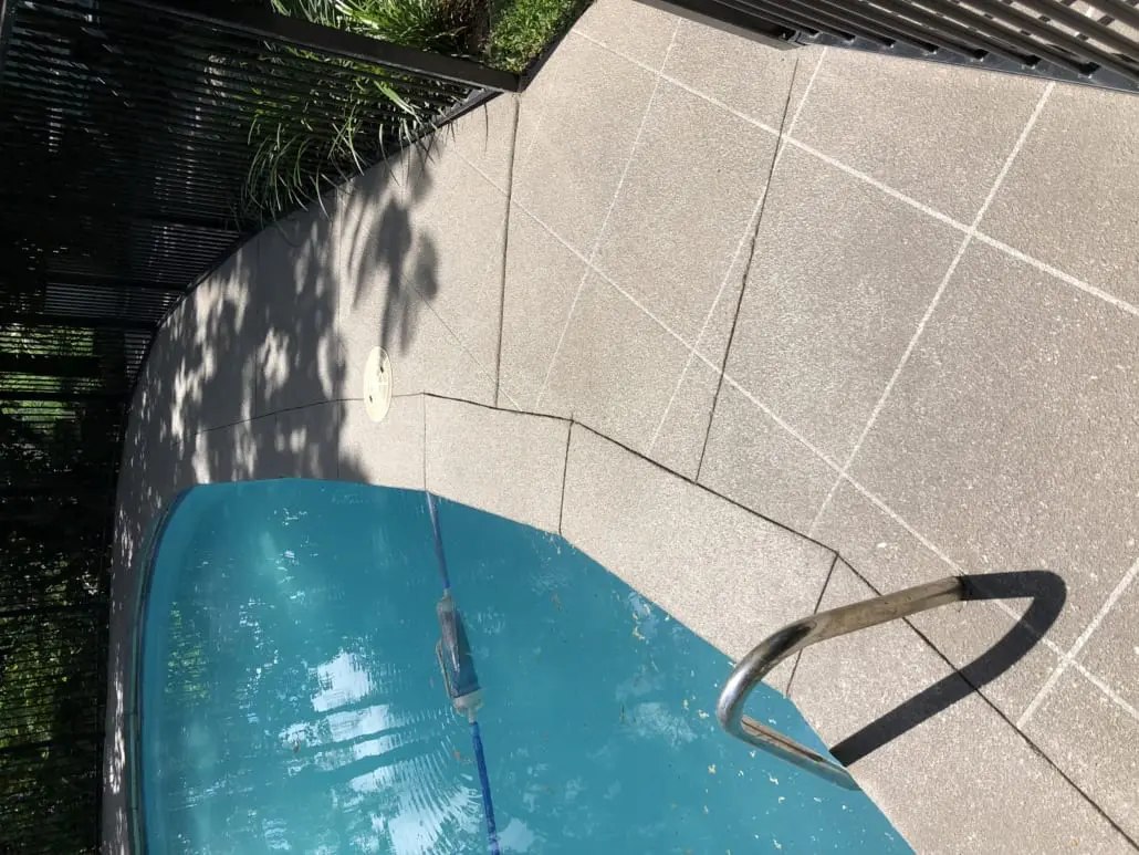 Speckled grey concrete pool surround resurfaced with fine saw-cut joint lines around a backyard pool